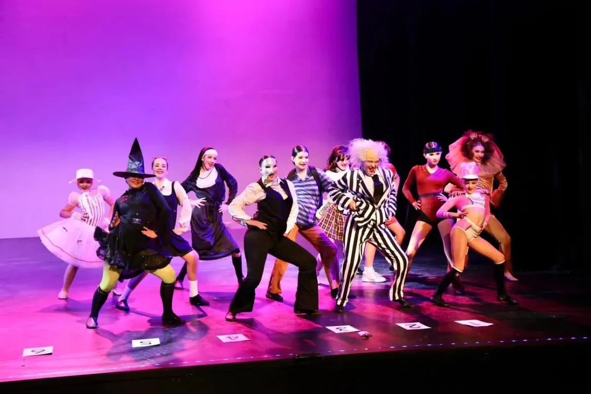 Teen performers in character costumes pose mid-scene on stage during a musical theatre performance, bringing storytelling, expression, and triple-threat talent to life in our recreational program.