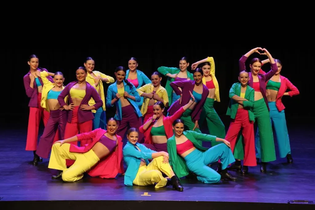 A confident tap group of young adult dancers in colourful, semi-formal suits striking a pose on stage, capturing rhythm, style, and the joy of performing in our recreational tap program.