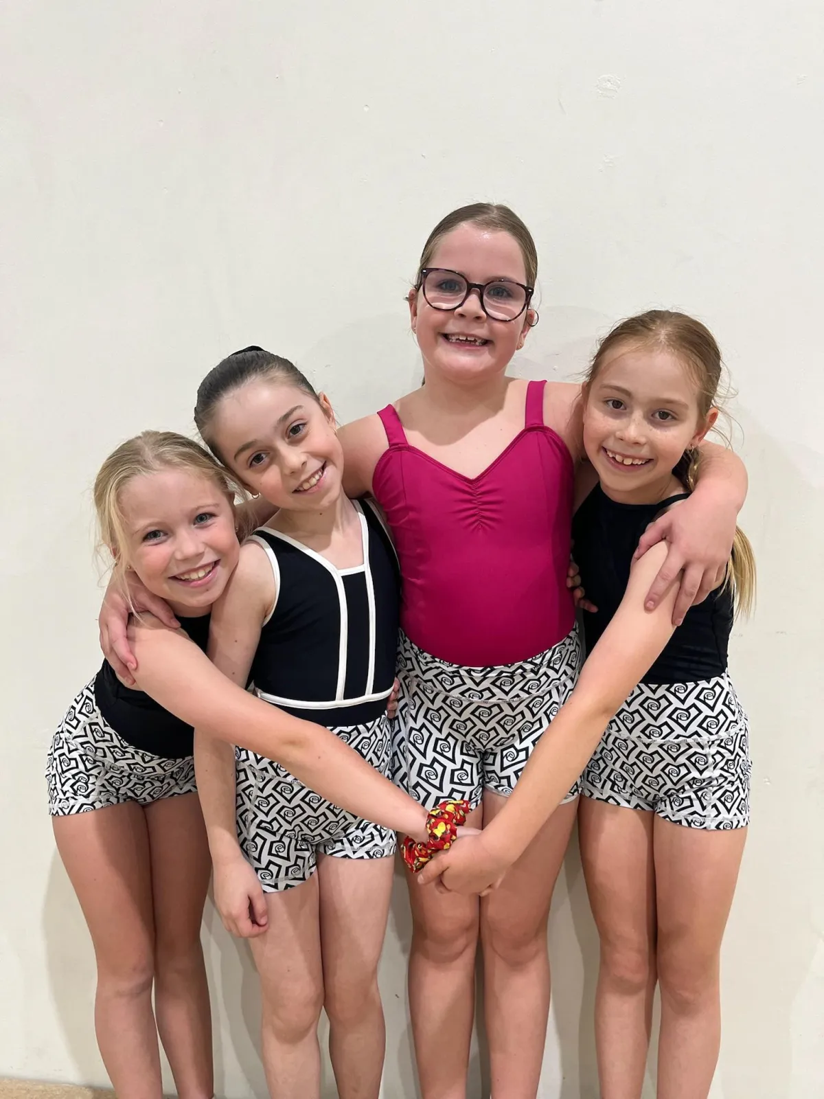 Four young dancers wearing matching shorts form a heart shape with their arms and smile brightly, celebrating connection, joy, and shared love of dance at The Star Factory Joondalup.