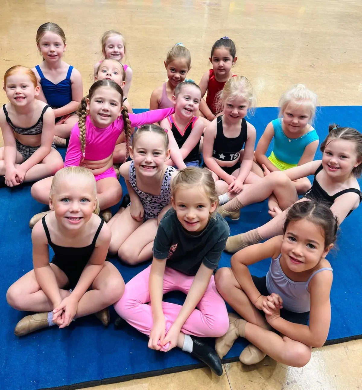 A cheerful group of girls sitting on mats smiling together after a dance class at The Star Factory Joondalup, highlighting the welcoming, inclusive, and uplifting environment of our kids’ dance studio.