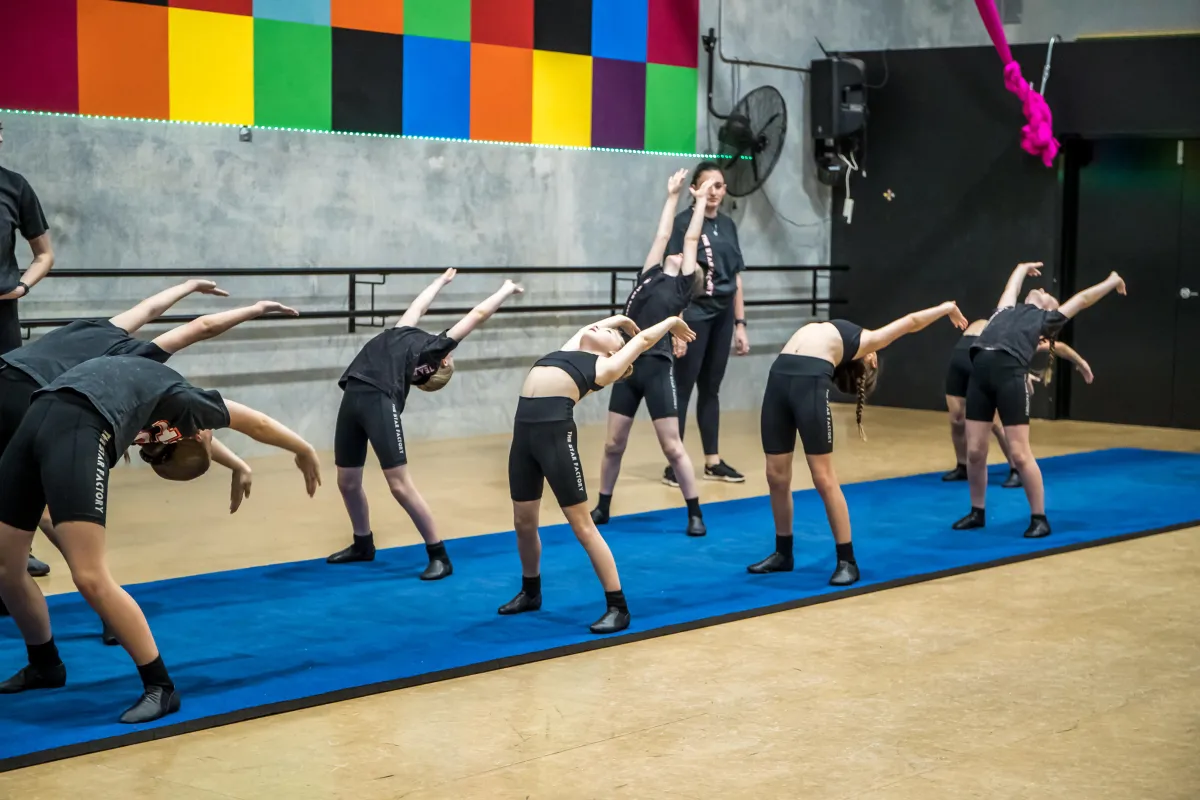 Two lines of girls confidently bending backwards during an acro class at The Star Factory Joondalup, with a teacher observing, capturing strength, flexibility, and trust in our recreational and elite acro training.
