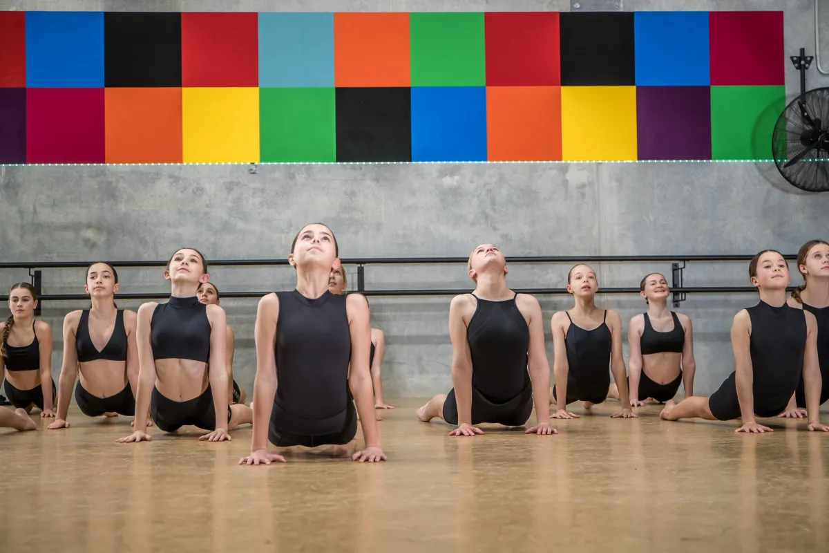 Teen dancers in black clothing stretch confidently on the floor at The Star Factory Joondalup, emphasizing strength, posture, and discipline developed in our dance conditioning classes.