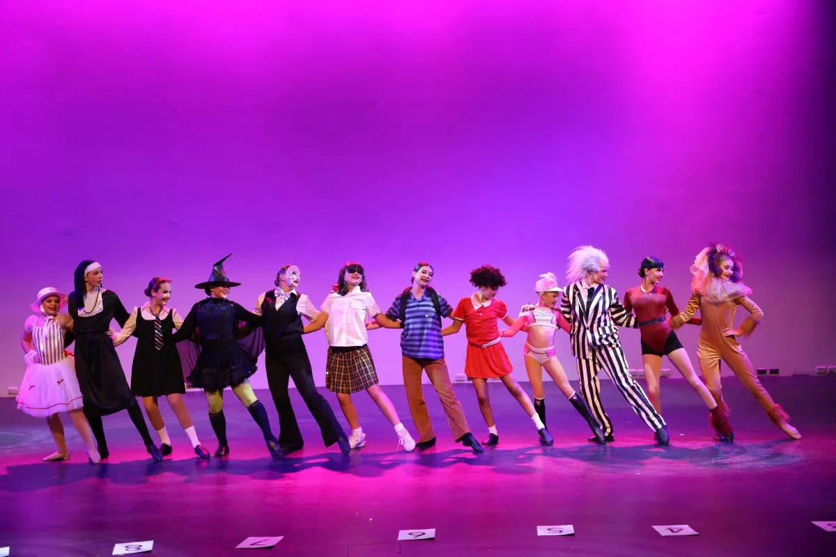 Teen performers in character costumes pose in a classic musical theatre chorus line on stage, celebrating stage presence, storytelling, and the triple-threat training offered at The Star Factory Joondalup.