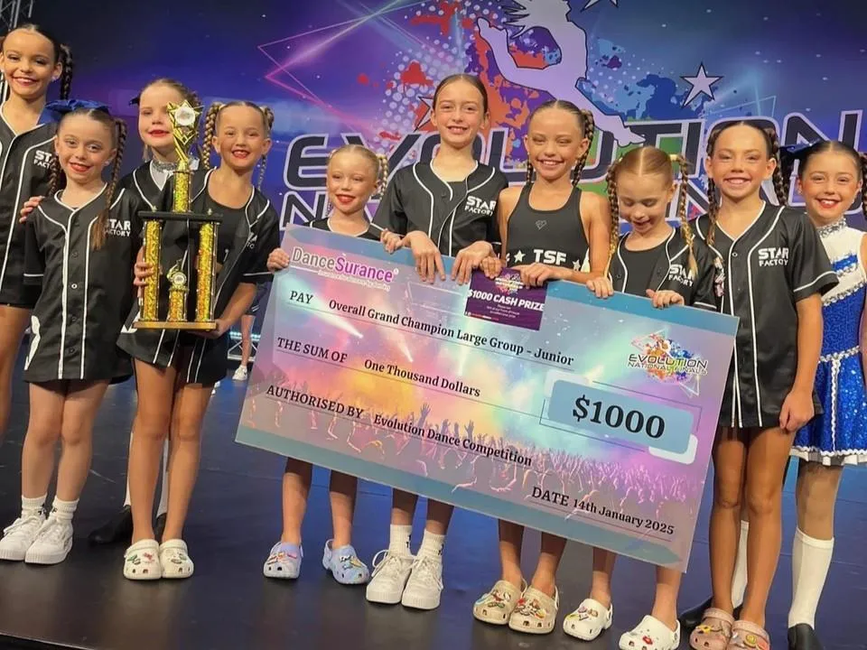 Dancers in black costumes proudly holding a championship trophy and winner’s certificate after a competition, representing the excellence, dedication, and success of The Star Factory Joondalup’s elite performance teams.