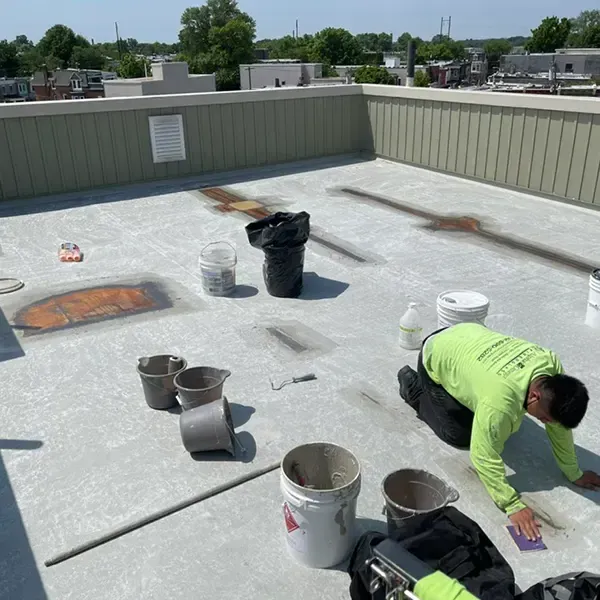 Fiberglass roof repair in Philadelphia, worker applying sealant to roof surface and patching seams.
