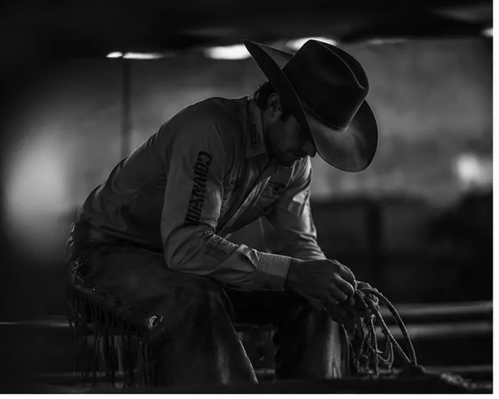  A gritty, high-contrast black and white image of a rodeo athlete performing a dynamic workout next to a dually truck and horse trailer, emphasizing the raw athletic nature of off-the-dirt training.