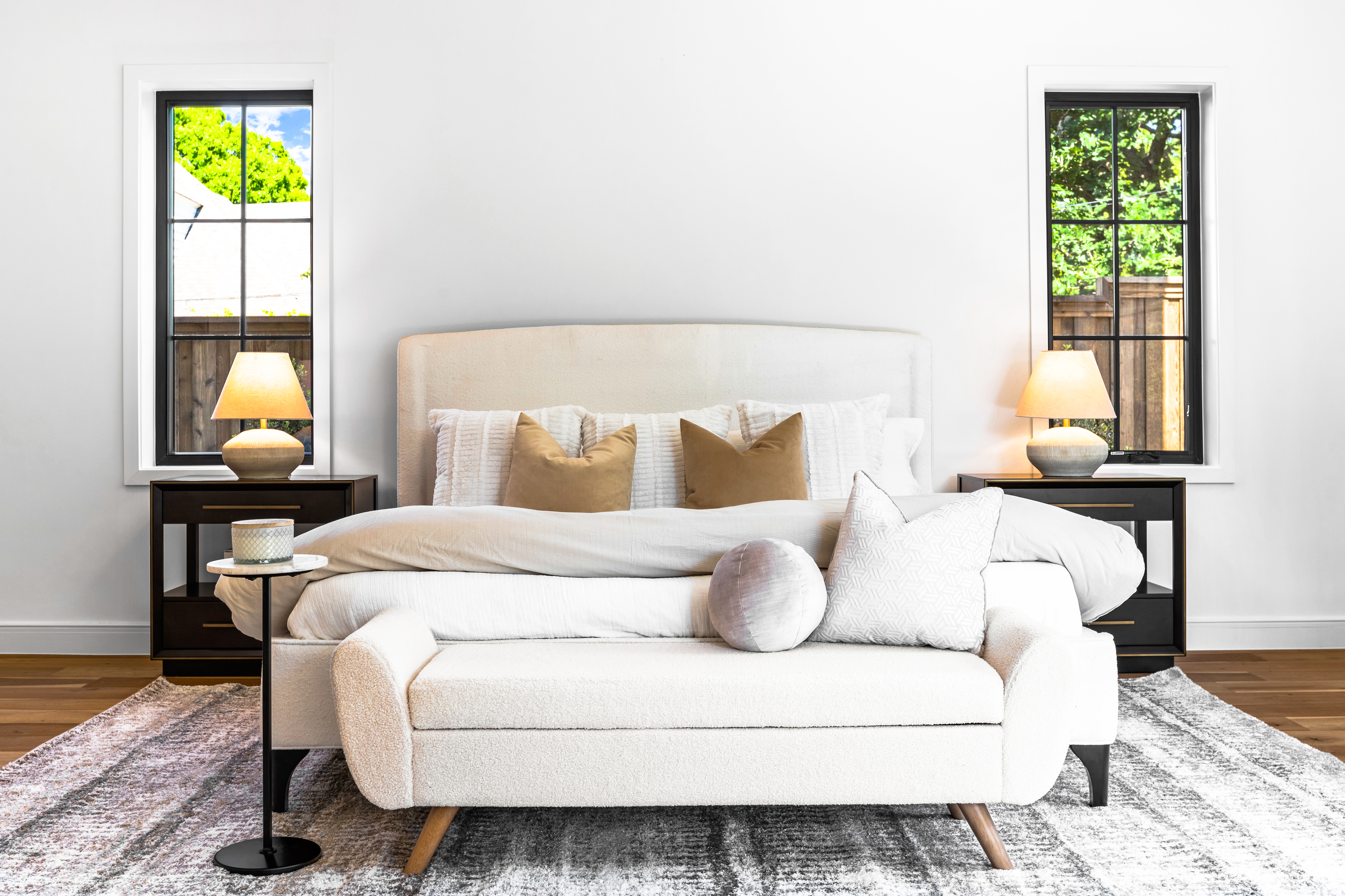 Bright all-white bedroom with a cozy sitting area at the end of the bed, professionally staged by Model My Home—Dallas Fort Worth home staging and interior design experts.