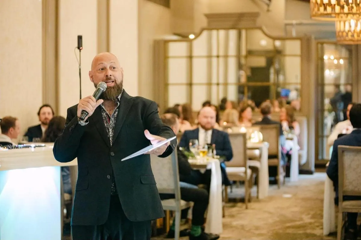 DJ Joe The Sounds DJ Services holding a microphone and MCing a wedding reception in a ballroom full of guests