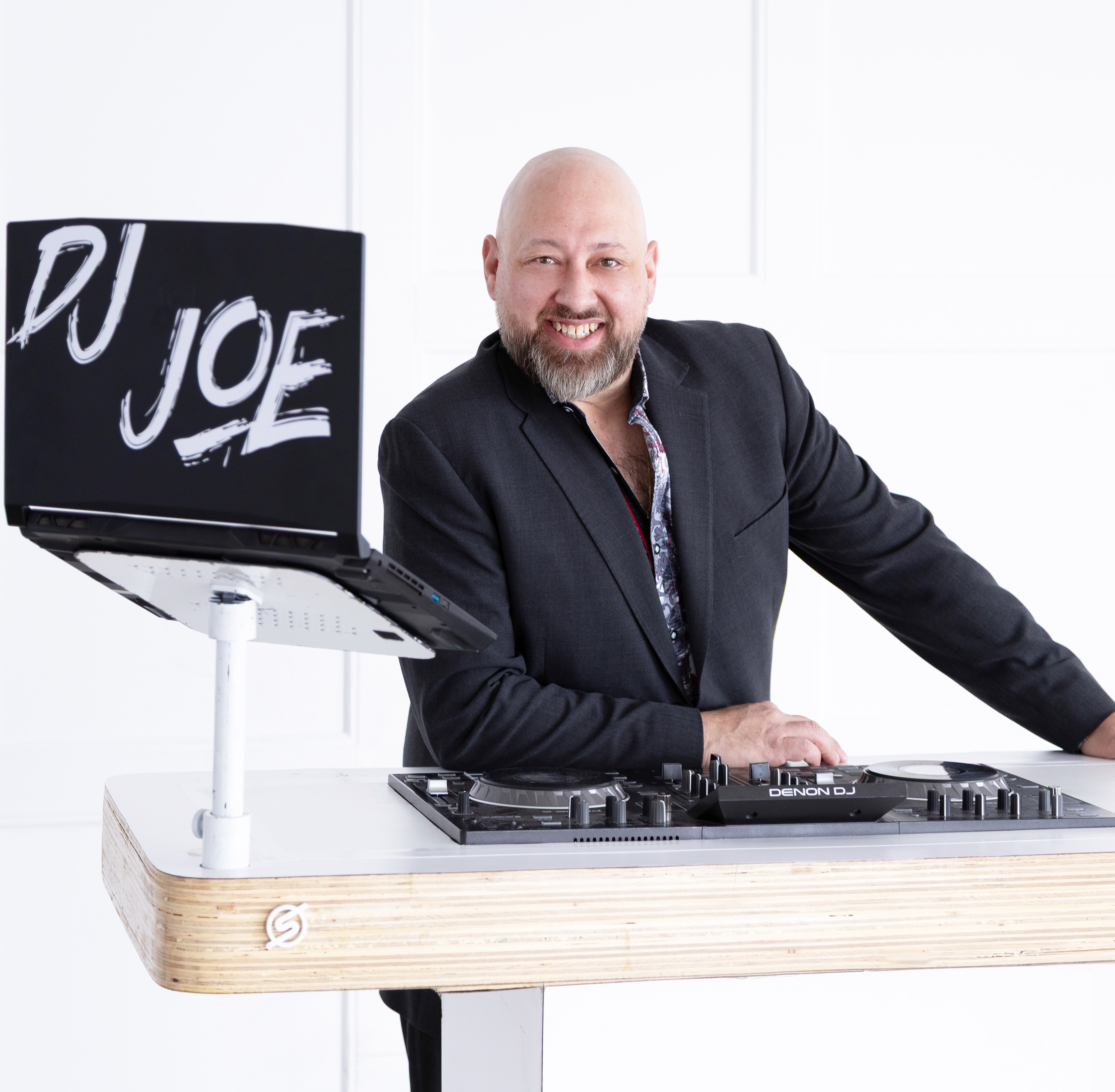 DJ Joe, owner of The Sounds DJ Services & Entertainment, smiling beside his professional DJ booth.