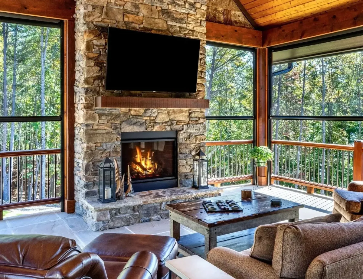MaxForce hurricane screens enclosing rustic residential outdoor living room with stone fireplace, wood-beam ceiling, and pool view