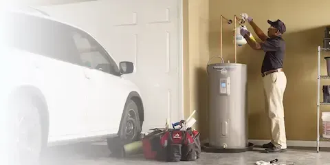 Technician servicing water heater unit in residential garage