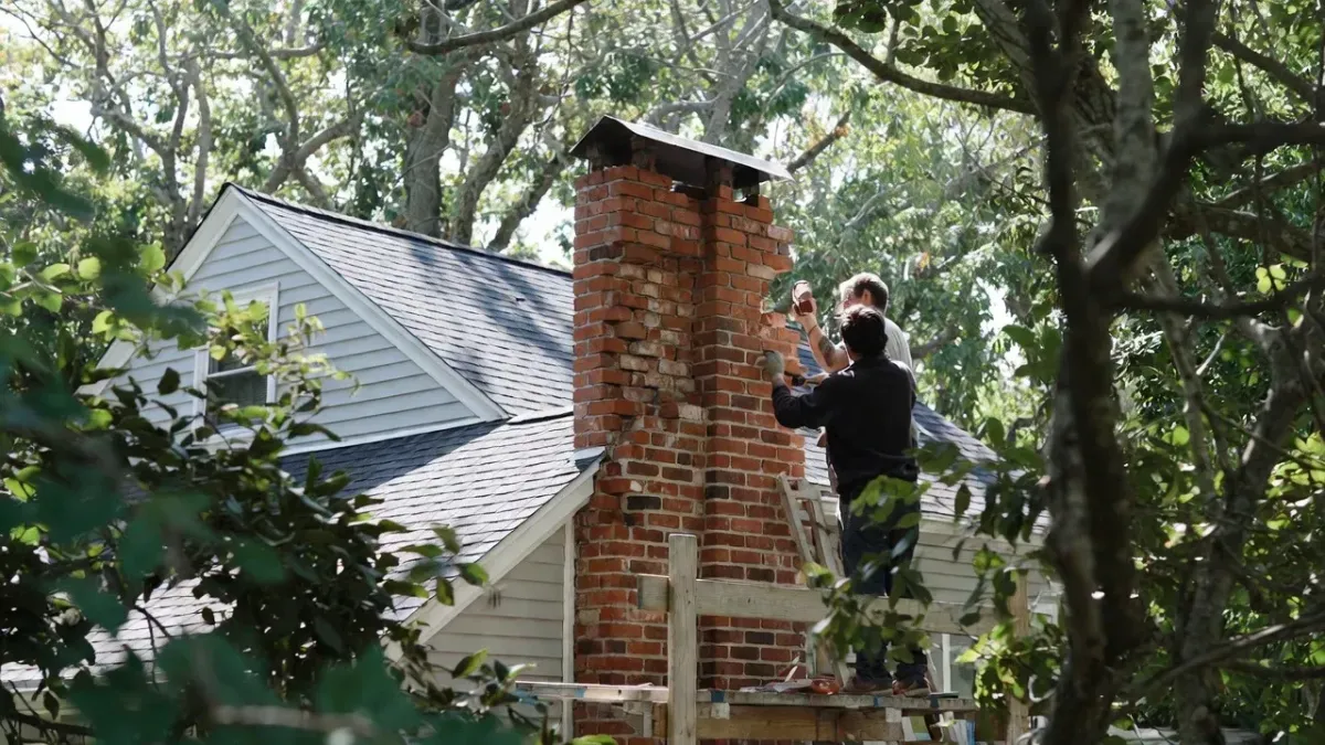 Chimney repair project in Newburyport MA with two-man masonry crew working on brick chimney using scaffolding