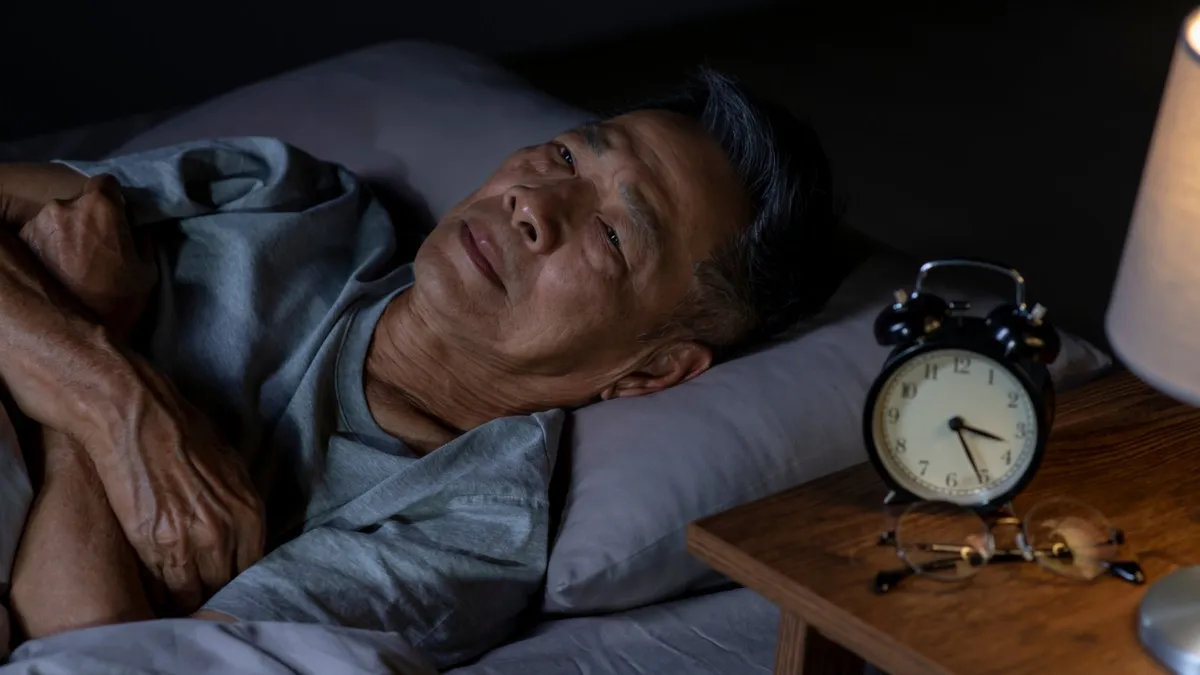 Older man asleep next to a bedside alarm clock