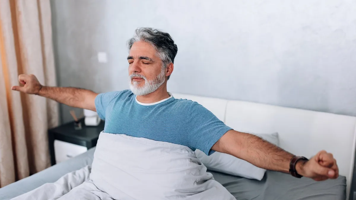 Older man stretching as he wakes up in bed
