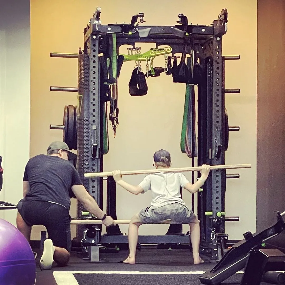 Coach guiding an athlete through an overhead dowel squat to assess thoracic mobility