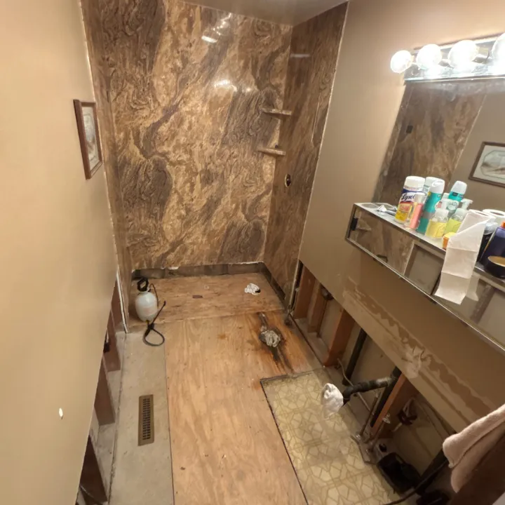 Bathroom water damage repair in Omaha with flooring removed, exposing stained subfloor near the shower and vanity