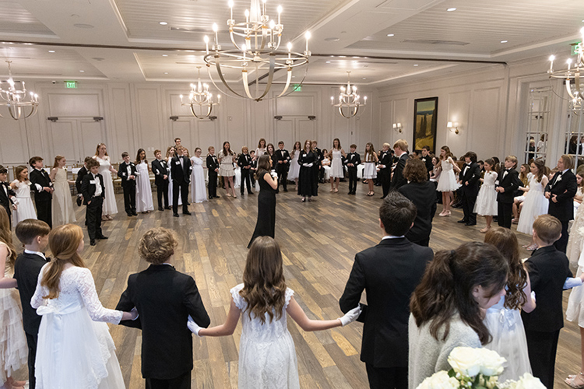 Young ladies in formal white dresses, Gentlemen in Black Tie Tuxedos arm and arm at Grand Ball.  