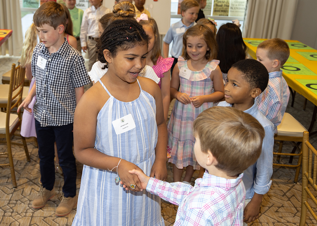 Young lady and gentlemen students shaking hands meeting each other for the first time while smiling and making good eye contact.  During Pre-Cotillion Manners and Etiquette class Richland County Club Nashville TN NLJC Grades 1-5