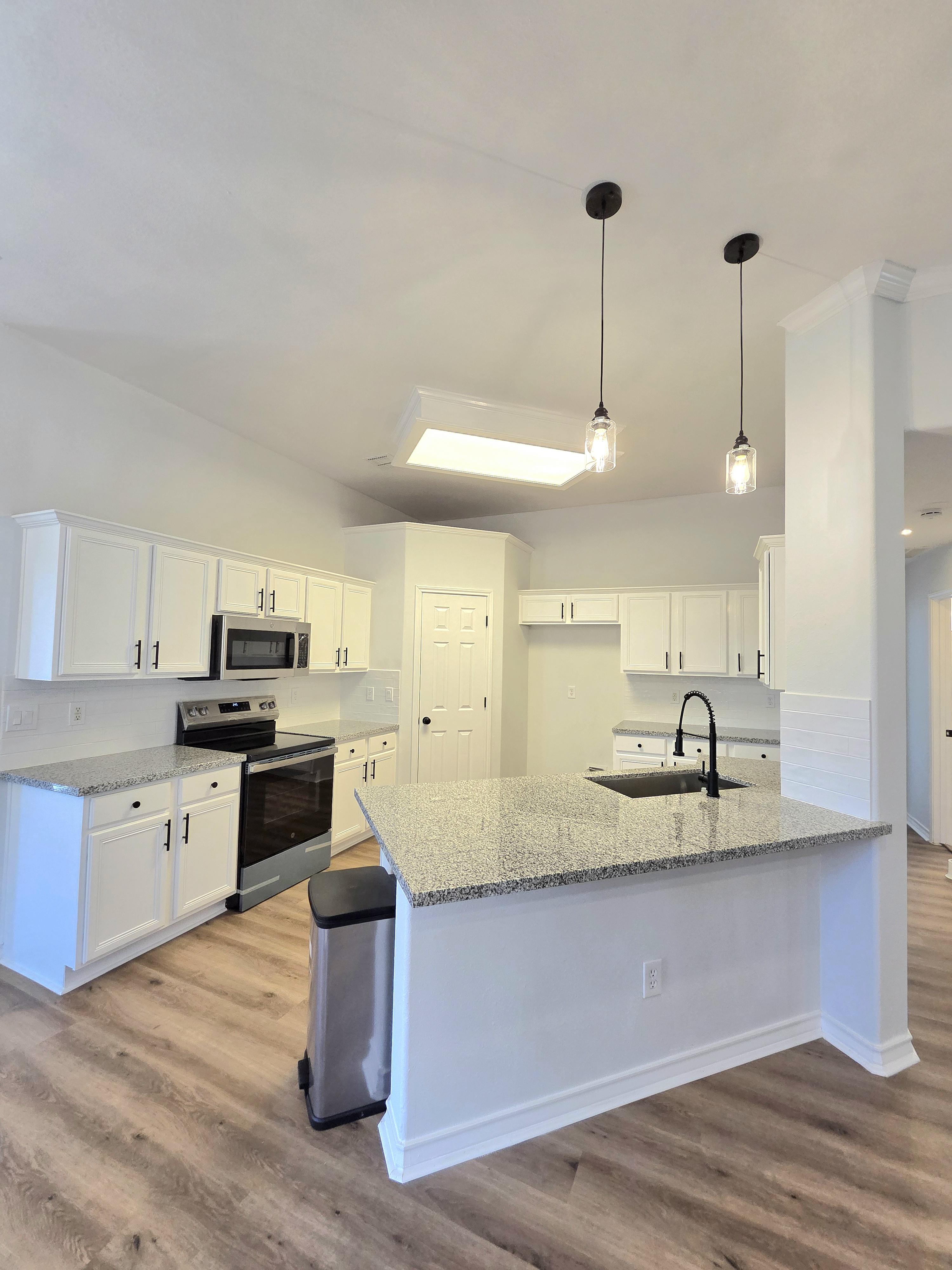 Modern kitchen with quartz countertops, stainless steel appliances, and a large island. The kitchen is illuminated by pendant lights and features sleek cabinetry, perfect for cooking and gathering with family in Corpus Christi.