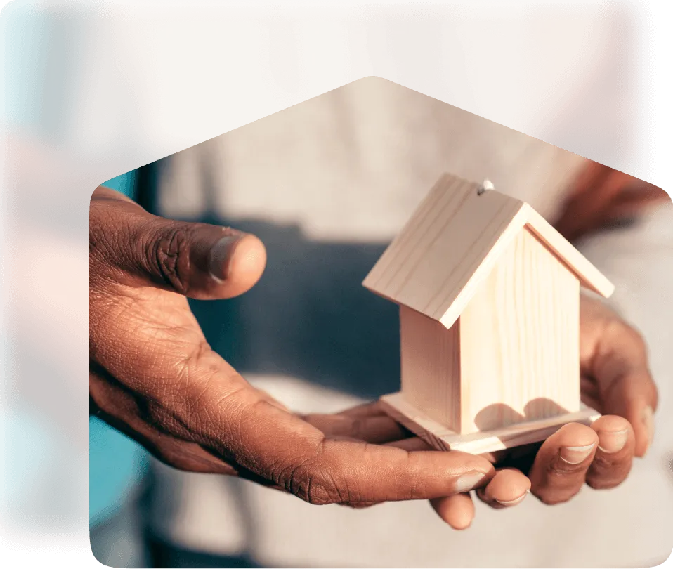 An aspirational image of the hands of new home owners holding a small wooden model house in their hands, symbolizing achieving home ownership through New Beginning's lease-to-own program