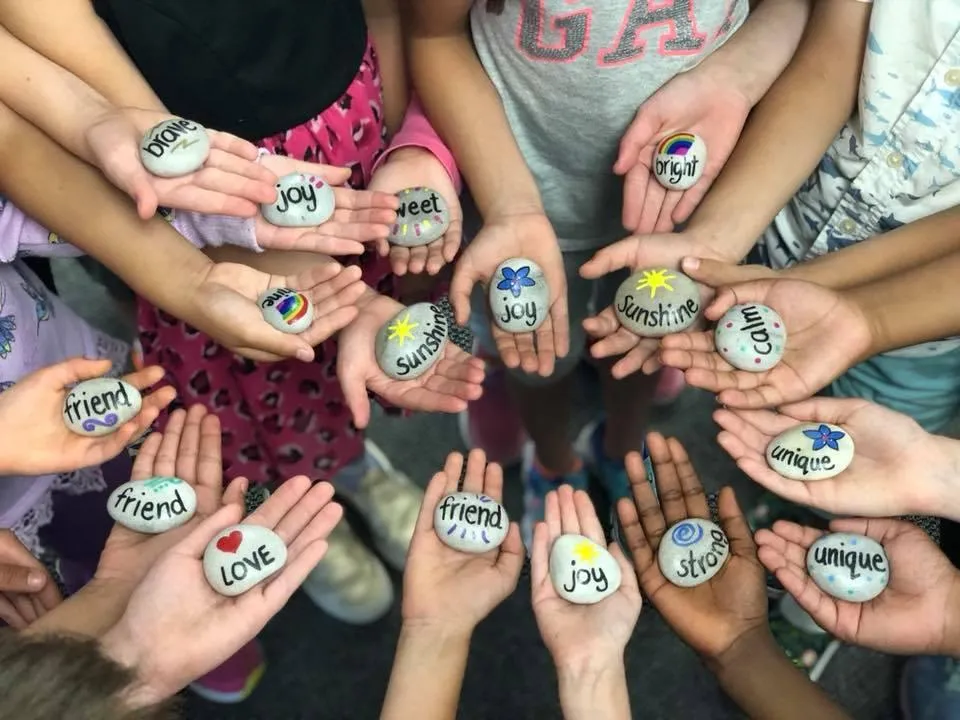 Photograph of children's hands in a circle holding painted meditation rocks.