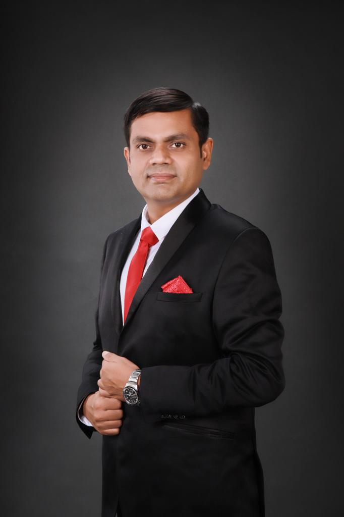 Dr. Saurabh Chaudhuri portrait in warm spiritual study with subtle Himalayan backdrop