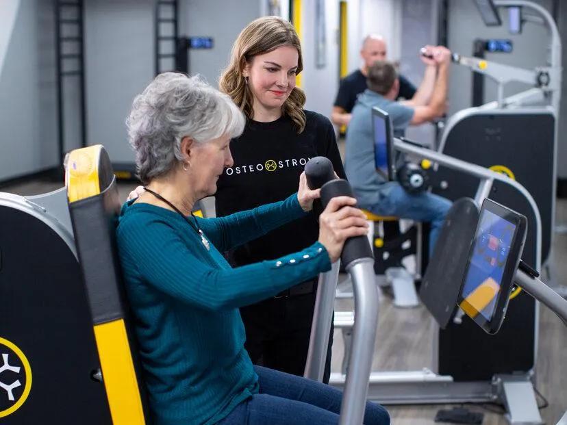 Woman using the OsteoStrong Spectrum System with a coach for bone strength and Osteogenic Loading