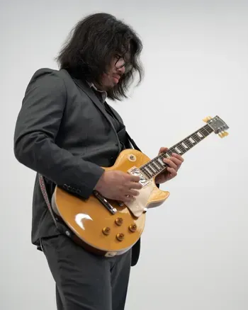 Lead guitarist in black jacket holding a gold electric guitar