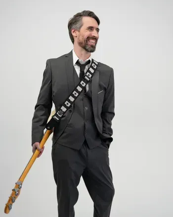 Bassist in a dark suit holding a bass guitar
