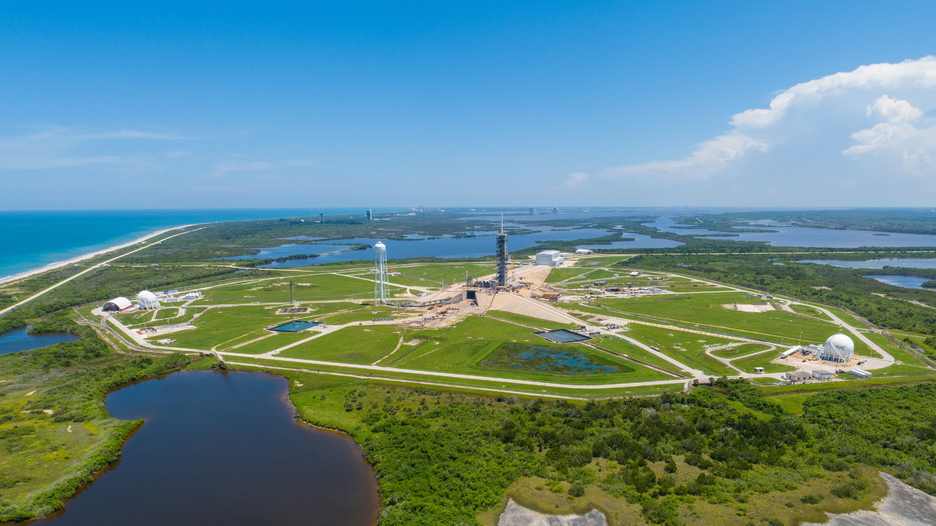 Aerial view of Cape Canaveral's launch complex at sunrise, with a rocket on the pad reflected in the surrounding waterways, representing the next era of global infrastructure investment."