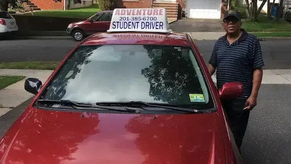 Driving instructor standing beside a compact instructor vehicle on a tree-lined suburban street at golden hour.