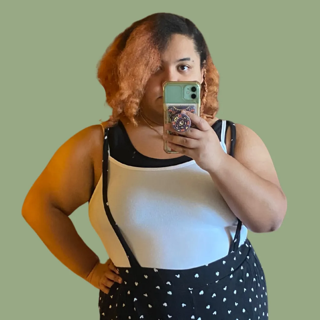 A circular picture of Hunter Archield-Cupit with orange and black hair in a white tank top and black pants with suspenders. There is also a light moss green background.