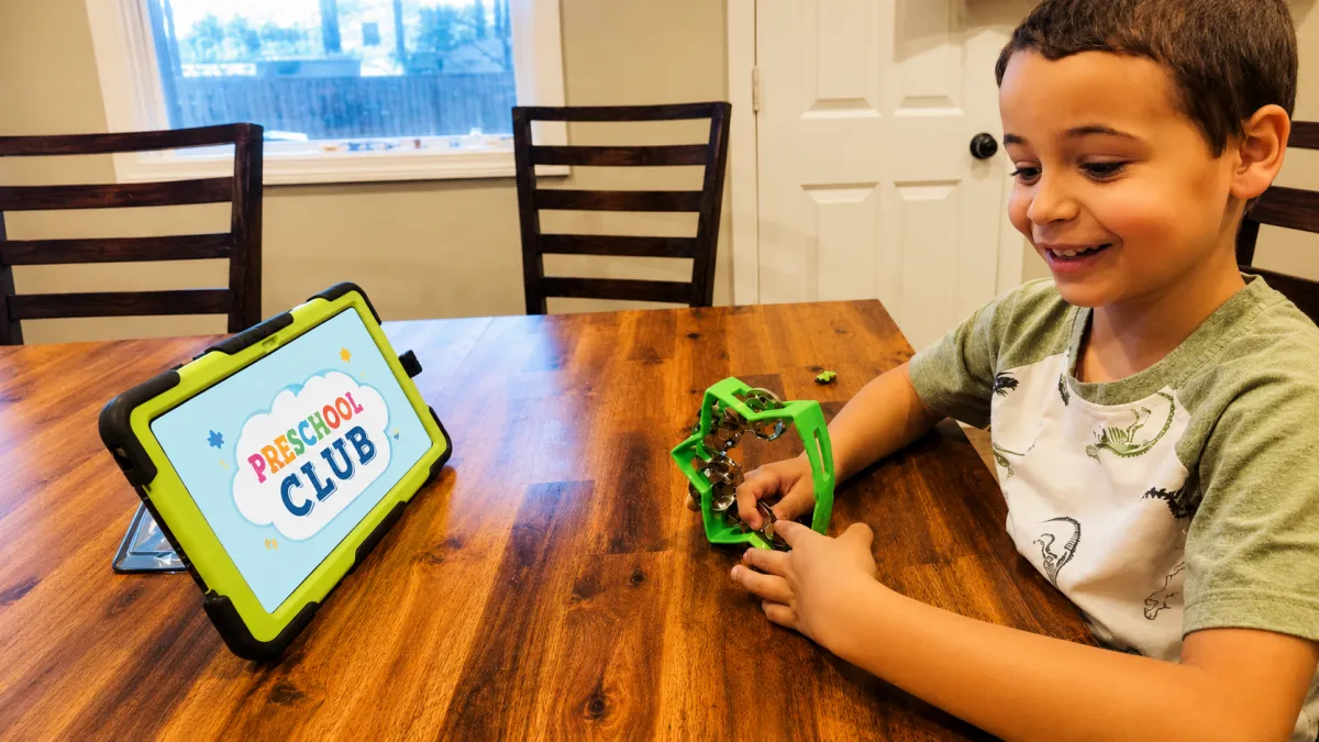 Boy holding a tambourine while watching the teacher on his tablet