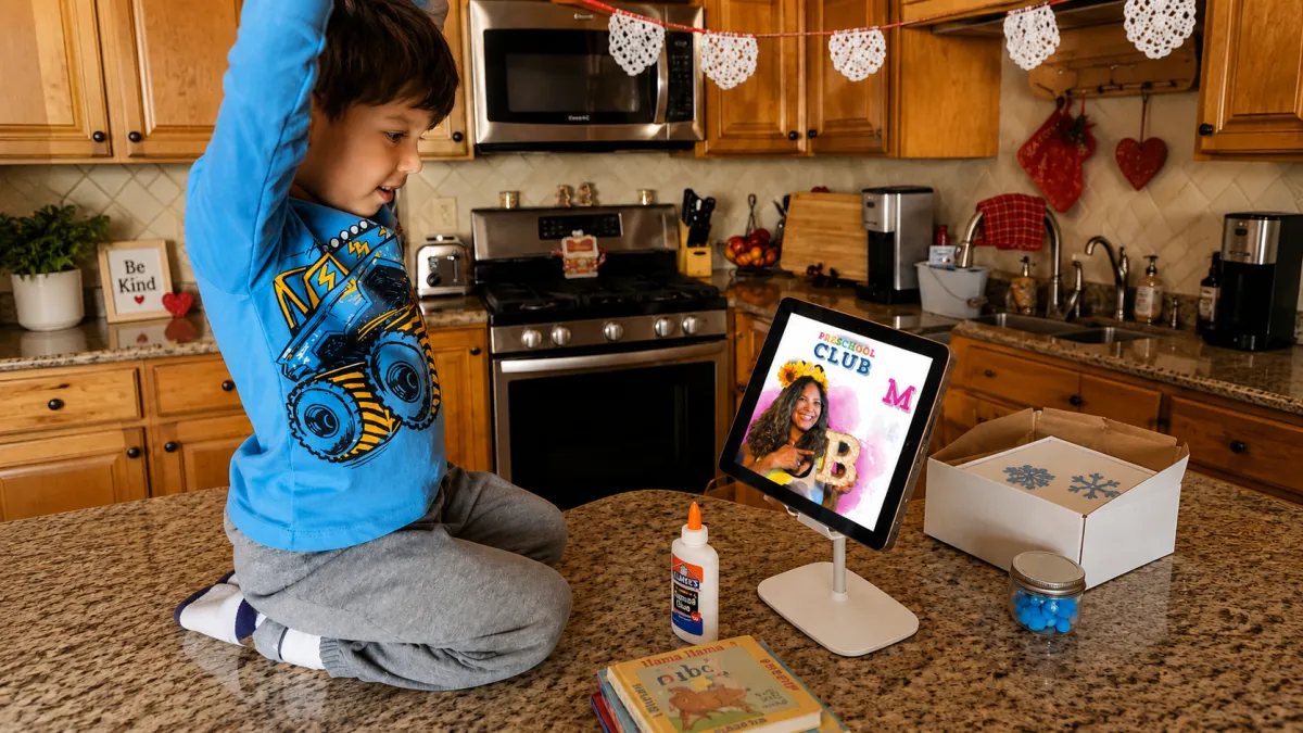 Boy sits on the kitchen counter watching the teacher on his tablet.