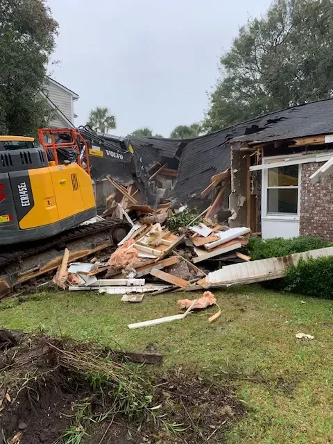 Demolished house in Myrtle Beach with organized debris, construction barriers, and palm trees under a clear blue sky.