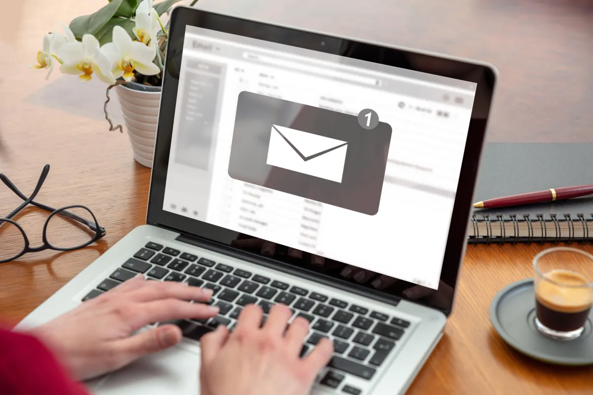 Person is looking at their email inbox while works on laptop displaying the icon of a white envelope on a gray background marked with the number one.