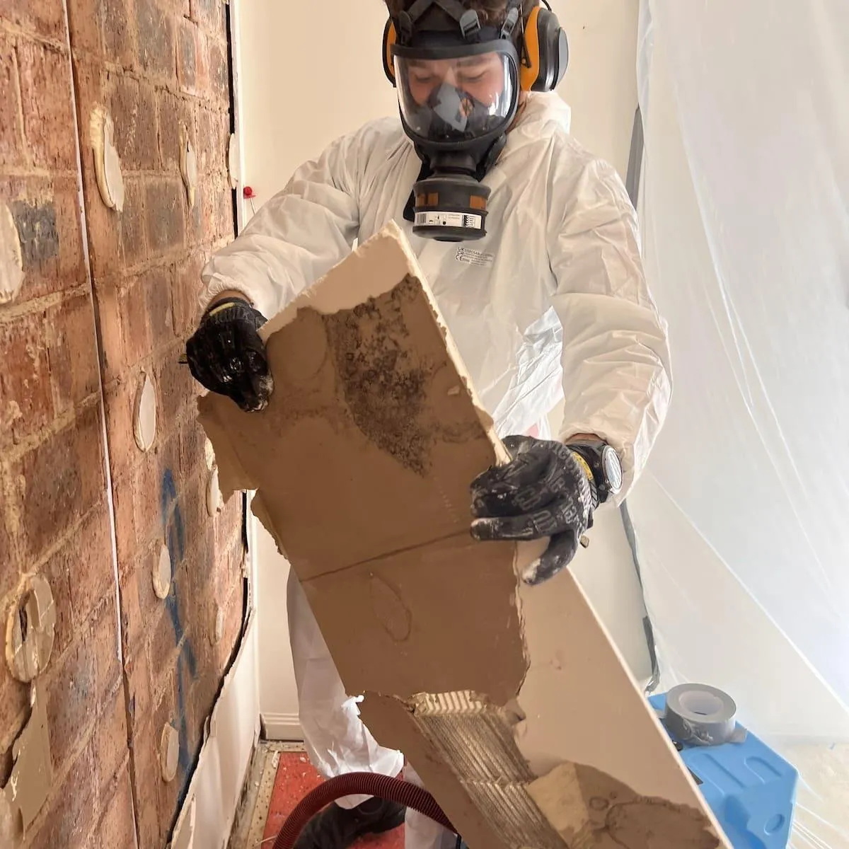 Technician in protective gear removing damaged wall material after water ingress, showcasing High Demand Restoration’s professional flood and mould remediation process in Sydney.