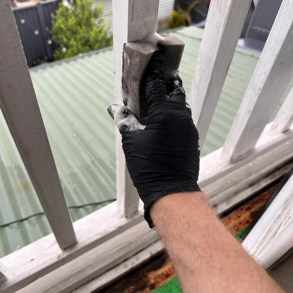 Technician cleaning mould from exterior window frame using protective gloves.