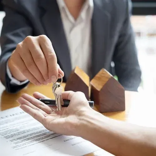 Agent handing over house keys to new property owner at office desk.
