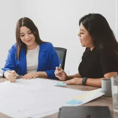 Two women collaborating over strata management plans in meeting room.