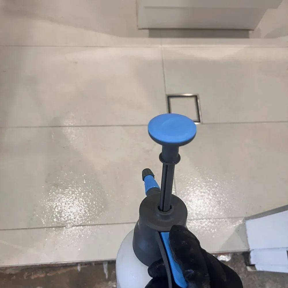 Technician disinfecting tiled floor using sprayer after sewage cleanup.