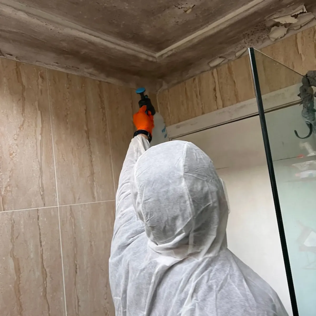 Technician in protective gear performing mould removal on a bathroom ceiling, demonstrating High Demand Restoration’s thorough cleaning and remediation process.