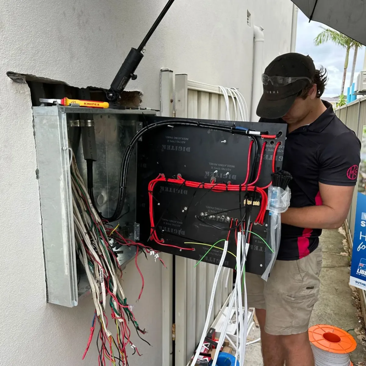 Electrician inspecting a damaged switchboard and electrical cabling, highlighting High Demand Restoration’s professional electrical repair and fault restoration services.