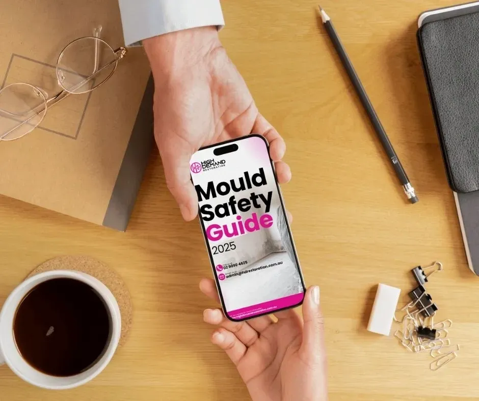 Person holding a Mould Safety Guide booklet on a desk with coffee, symbolizing High Demand Restoration’s free mould education resource for Sydney homeowners and property managers.