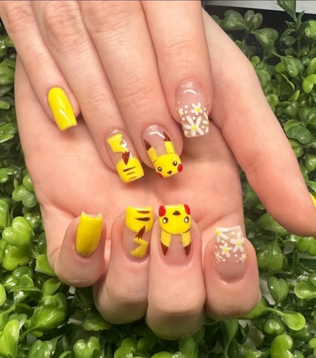 A set of Pokemon inspired nails, the pinky and thumb are solid yellow, one nail has white flowers, the final two nails have Pikachu, one contains his head and the other contains his tail