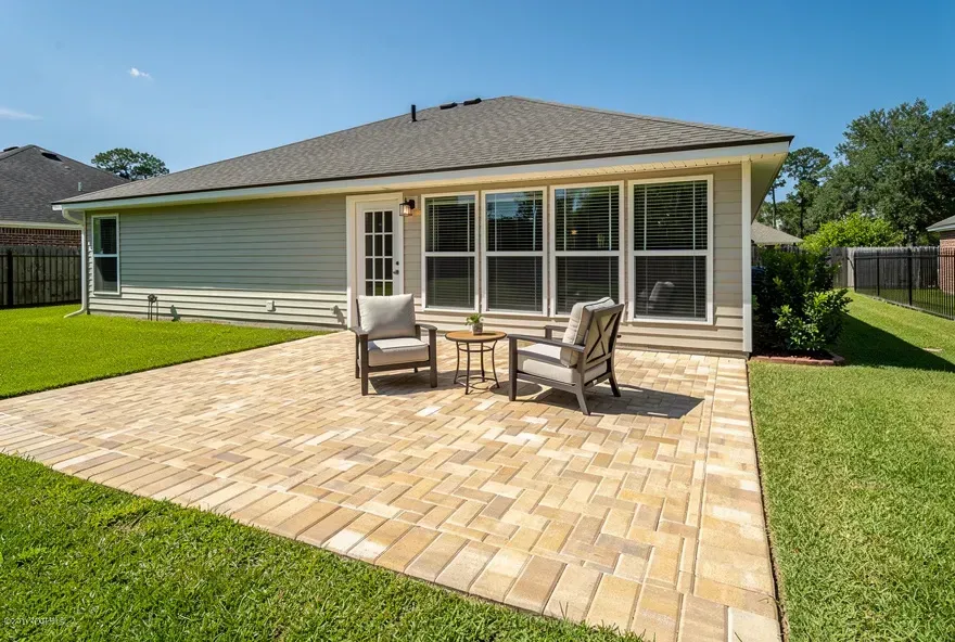Finished tan paver patio attached to a modest Denham Springs home with outdoor furniture on a sunny day