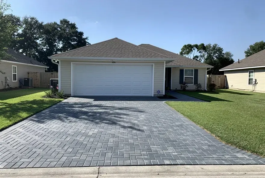 Gray paver driveway connected to garage of a modest Denham Springs home on a sunny afternoon