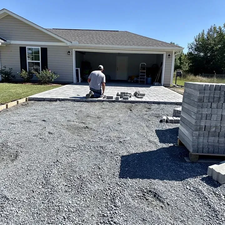 Paver driveway installation in progress near a garage entrance in Denham Springs with worker laying stones in the distance