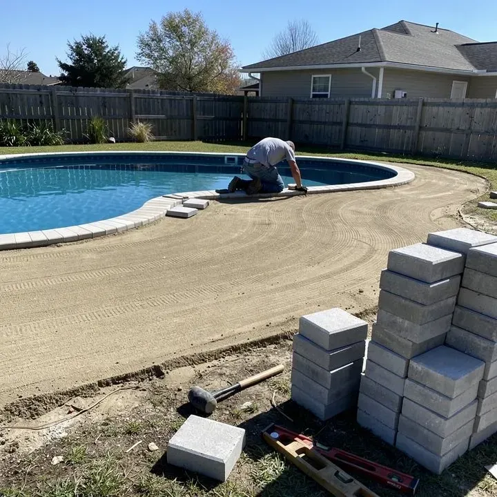 Paver pool deck installation in progress near pool edge in Denham Springs with worker laying stones in the distance