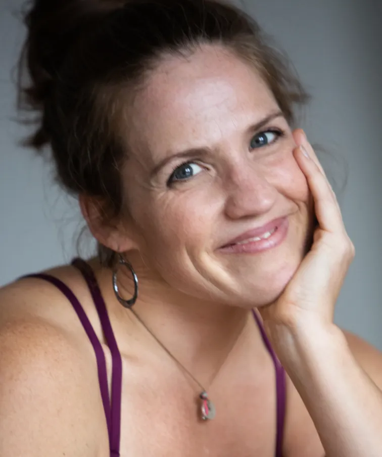 A professional portrait of Erin LoPorto, smiling warmly in a sunlit studio. She wears casual, comfortable attire and exudes approachability and expertise. The background is softly blurred, focusing attention on her friendly expression and confident posture.